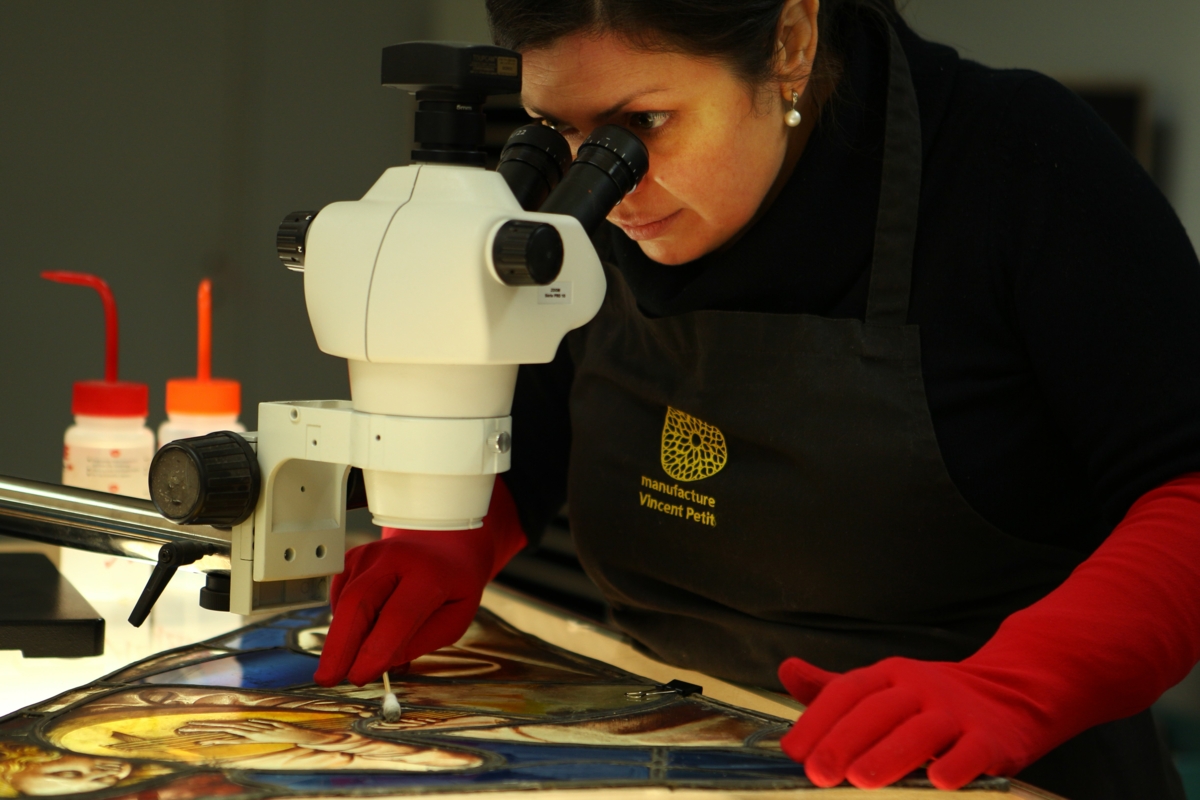 Une femme regarde dans un microscope et passe un coton tige sur un vitrail.